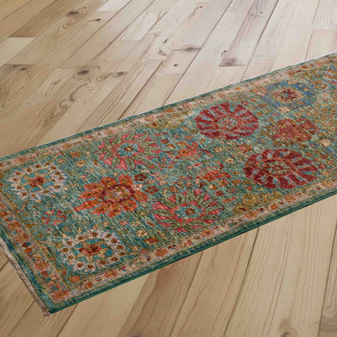 A long runner with a distressed traditional pattern in teal, amber, crimson, and pale gold, shown laid out diagonally on a light wood plank floor.