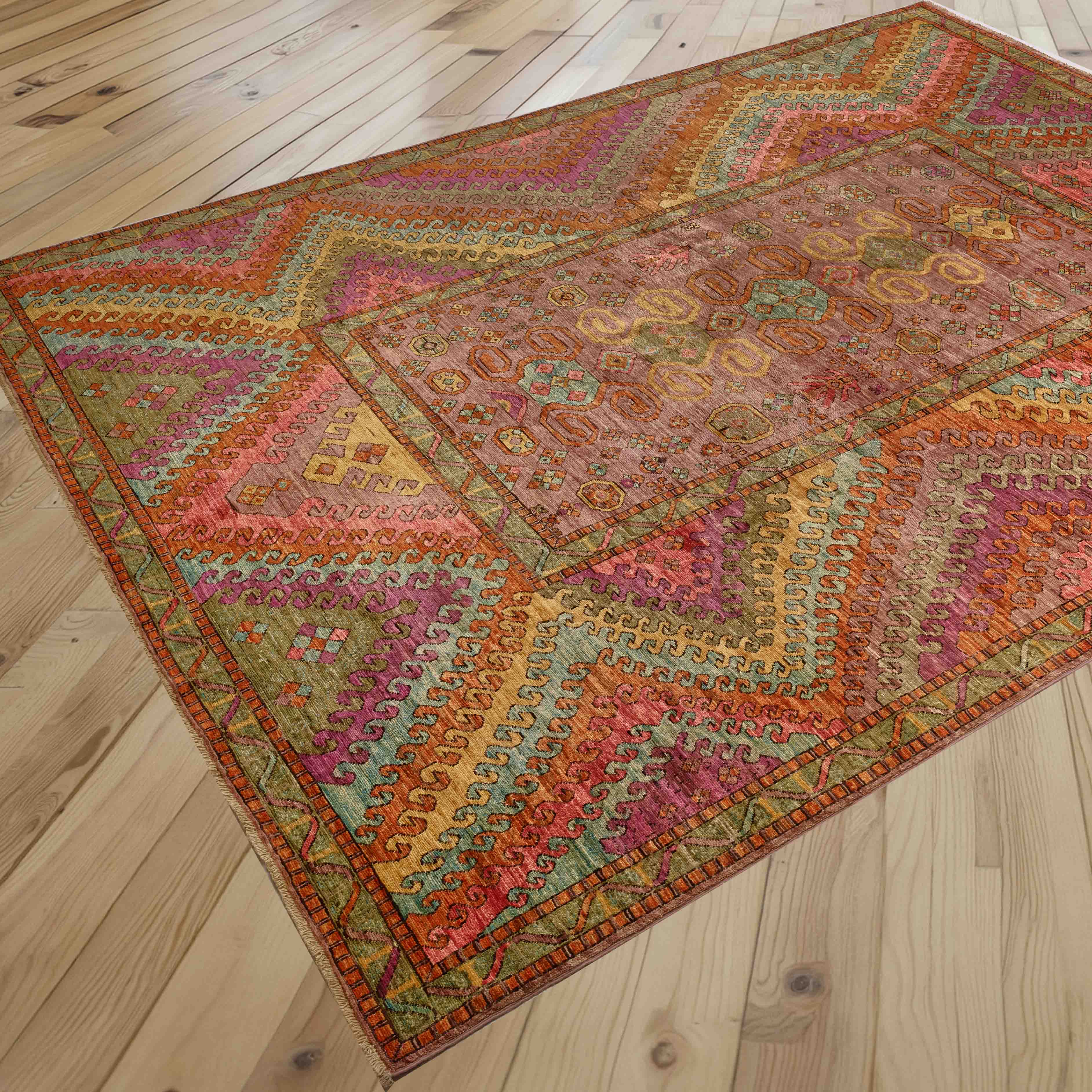 A rectangular area rug with a complex geometric and tribal pattern in multiple warm colors, displayed on a light-colored wooden plank floor.