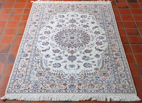 This Nain measures 162 by 109 centimetres.  With a colour palette of cream/ivory background with different shades of blue in the design and tiny touches of a deep burgundy red as an accent colour.   The decoration consists of a complex floral pattern  around a central medallion, the centre of which is a beautiful, delicate flower. This rug has almost a mushroom pink border.