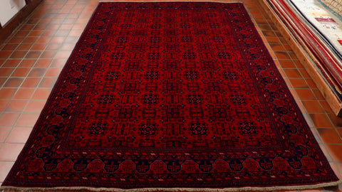 There is a symmetrical design of a network of interlocking motifs across this rug, all of the decorative work is in deep blue with highlights in white.  There is a border made up of thinner bands of decorated bordeer complimenting the central section.  The ground to this rug is a depp raspberry red. 