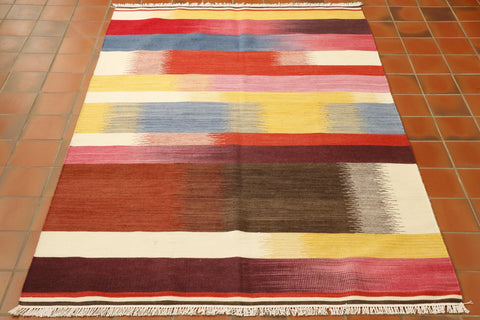 This Indian Kilim rug has bands of blended colour of varying width going across it horizontally.  These bands are burgundy/pink, tans and browns, reds and oranges, yellows and blues.  They blend from light to dark in different directions. 